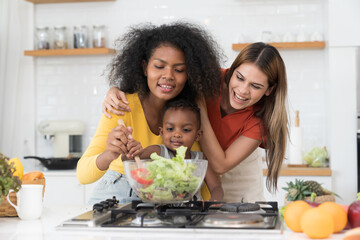 Two young woman and little boy cooking salad together in kitchen room at home