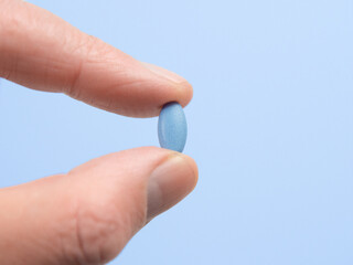 Blue pill for erectile dysfunction held between finger and thumb with a blue background.
