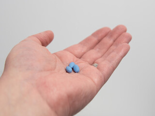 Hand holding blue pills for treating impotence or erectile dysfuntion
