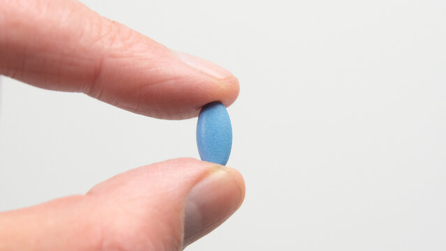 Blue pill for impotence or erectile dysfunction. Hand holding pill between finger and thumb.