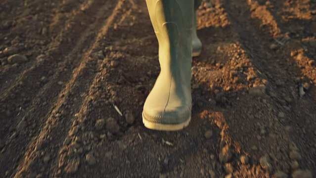 Farmer in rubber boots walking through tilled seedbed ready for sowing