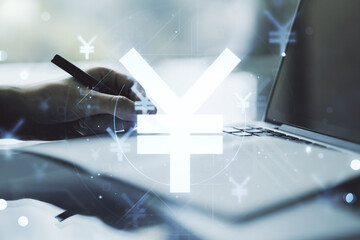 Creative concept of Japanese Yen symbol illustration and hand writing in notebook on background with laptop. Trading and currency concept. Multiexposure
