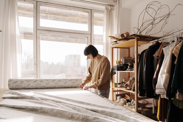 Artisan seamstress measuring fabric in sunlit sewing workshop with clothes and textiles.