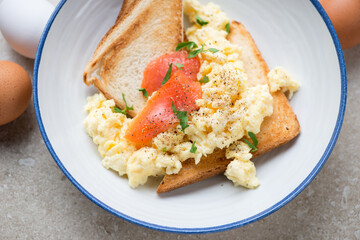 Toasts with scrambled eggs and smoked salmon in a blue and white plate, horizontal shot, middle closeup, selective focus