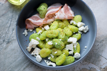Potato gnocchi with green pea sauce, feta and bacon in a grey bowl, horizontal shot, middle closeup, selective focus
