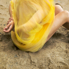 woman covered with a yellow tulle sitting on the sand of an Asturian beach III