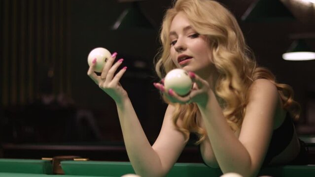 Blond woman playing enjoying billiard, hold billiard balls on table with green surface in billiard club. Pool game snooker pyramid player
