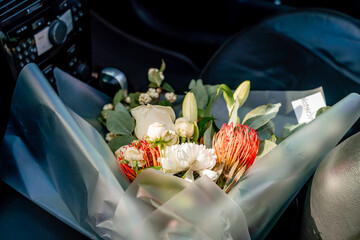 A bouquet of flowers is sitting in a car. The flowers are white and red, and they are in a clear...
