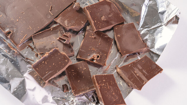 The chocolate bar is broken into pieces. Cocoa and chocolos on white background, concept of price increase for raw materials of chocolate production