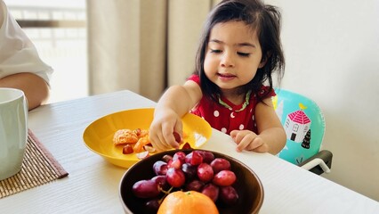 two year old girl eating fruit on her yellow plate for breakfast with her family