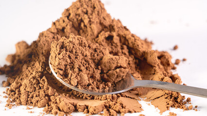 A spoon in cocoa powder in close-up. Cocoa is on the table and a spoon is poured.
