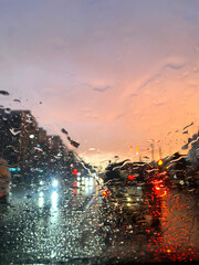Raindrops on the windshield of a car. Rain on the road. Sunset in the city. 