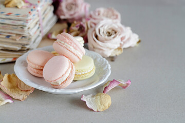 Fototapeta na wymiar French macaroons on the plate. Vintage letters and roses in the background.