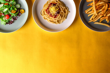 spaghetti with tomato sauce, salad and french fries kept on 3 plates on a yellow background