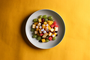 Fruit salad on a white plate kept on a yellow background