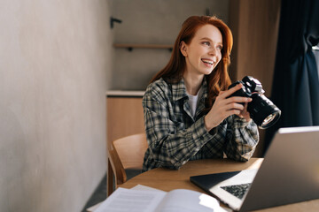 Cheerful female artist adjusting new professional photo camera or choosing photos for editing...