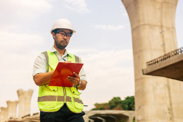 A man in a yellow jacket is writing on a clipboard while standing in front of a bridge. Concept of work and productivity