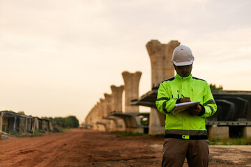 A man in a yellow jacket is writing on a clipboard while standing in front of a bridge. Concept of work and productivity