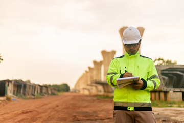 A man in a yellow jacket is writing on a clipboard while standing in front of a bridge. Concept of work and productivity