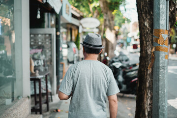 An adult man with grey hat is walking on the street with bokeh background