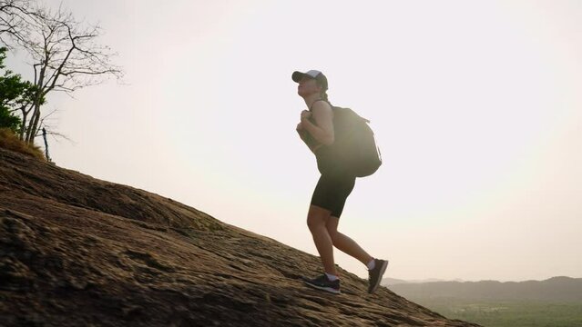 Active female hiker climbs steep mountain trail at sunrise, showing persistence, strength. Morning climb inspires, motivates with rich scenery, fitness adventure. Woman conquers Pidurangala Rock.