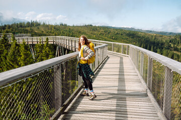 Fototapeta na wymiar Young woman on wooden bridge with backpack among treetops. Concept of freedom, travel, lifestyle. 