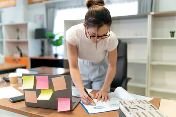 asian beautiful business woman writing paper. busy female professional employee write on paper sheet plan for other worker. an exhausted focus woman plan business by writing paper notes on the desk