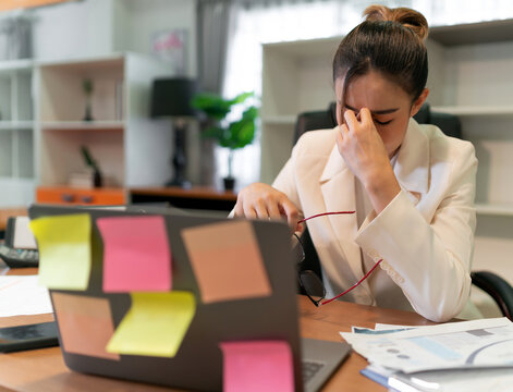 Stress business woman busy and pain from overwork. young adult Asian professional manager having office syndrome at office. beautiful employee upset in pain because working too much overtime work