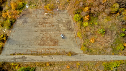 An old asphalt road winds through the forest in the mountains, surrounded by the golden canopies of autumn trees. This aerial photograph was captured by a drone.