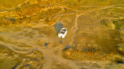 Traces of dirt roads and ruined houses mark the site of a former village, now submerged beneath the reservoir formed by a breached dam, with only the surviving church of St. Ivan Rilski, Bulgaria