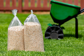 Bags of lawn fertilizer and herbicide with broadcast spreader in yard with healthy grass. Lawn...