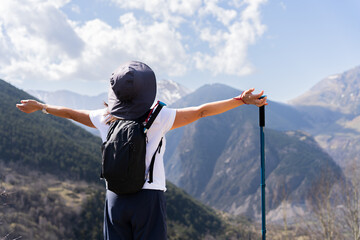 Unrecognizable woman with backpack and trekking pole opening her arms in front of a beautiful high...