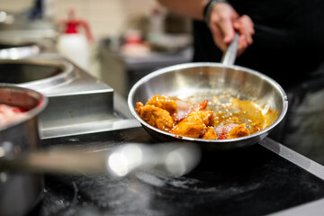 Dynamic culinary scene with a chef skillfully stirring a sizzling dish in a pan in a professional kitchen