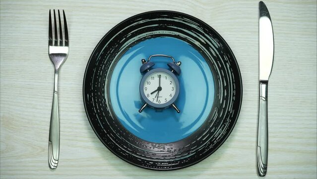 An alarm clock on an empty plate with fork and knife in the white table. Time to eat, Breakfast time. Weight loss or diet concept. Stop Motion