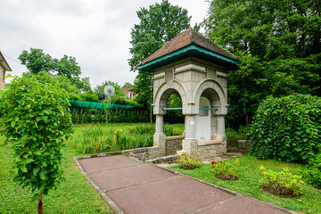 Fantana Jianu (Jianu Well) at the main entry to Alexandru Buia Botanical Garden from Craiova in Dolj county, Romania, and large green tres in a beautiful sunny spring day