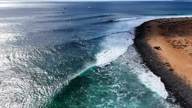 Flying over the coastline of Ponta Preta, Sal, Cape Verde. A big wave breaks. Kiters and surfers can be seen
