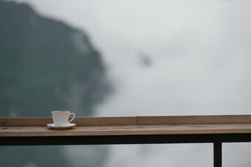 A cup of coffee sits on a railing with a foggy mountain view in the background, invoking a tranquil...