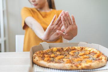 Diet concept, unhappy asian young woman, girl refusing to eat Pizza in box at home, hand pushing...