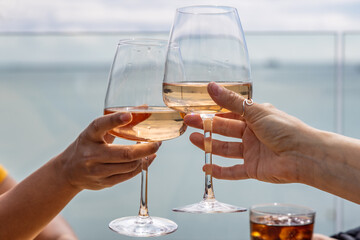 Wine glasses raised in a toast at an outside bar, with the sea in the distance behind