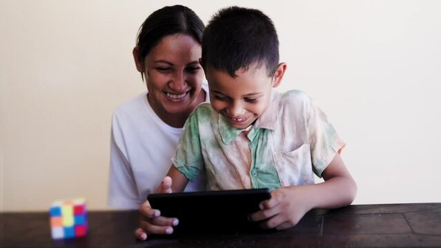 Latin mother and son having fun playing with tablet computer at home. Family relationship and technology concept