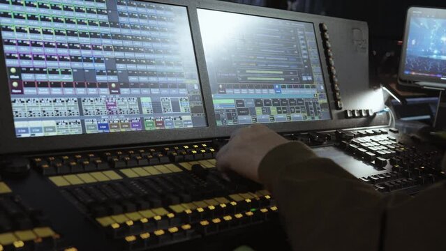 A lighting control desk is operated during a live event, showing a complex interface of controls and screens.