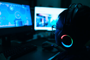 Young kid on the computer playing games, watching entertainment or browsing the online digital internet, young child wearing glasses and headset in the dark background theme.