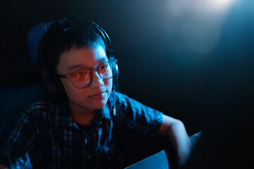 Young kid on the computer playing games, watching entertainment or browsing the online digital internet, young child smiling having fun wearing glasses and dark background theme.