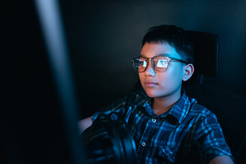 Young kid on the computer playing games, watching entertainment or browsing the online digital internet, wearing glasses and dark background theme.