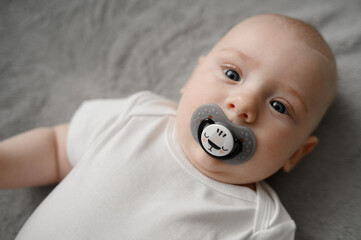Infant sucks a pacifier and looks at camera. Close-up of a baby with pacifier in his mouth lying on...