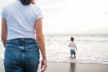 Mom and son Toddler are walking on the beach near the ocean. In the foreground is a silhouette of a...