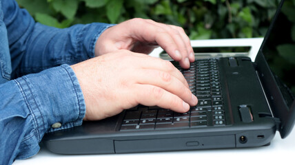 close-up hands of a man working on laptop in the garden of his house
