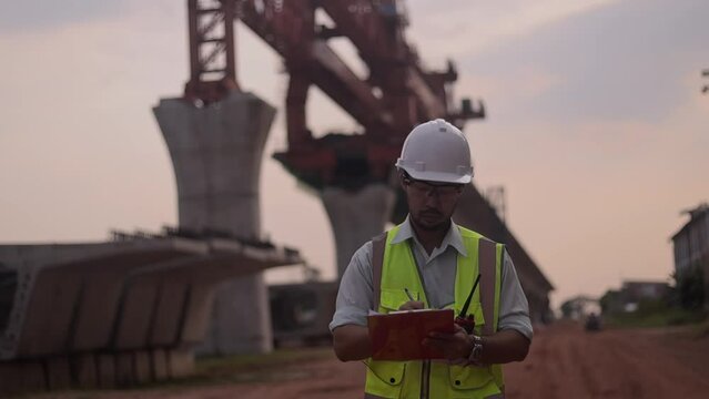 A man in a yellow jacket is writing on a clipboard while standing in front of a bridge. Concept of work and productivity