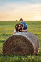 Naklejka na ściany i meble A happy family near a round roll of straw in a green meadow. The son is crouch high and watching his parents kiss
