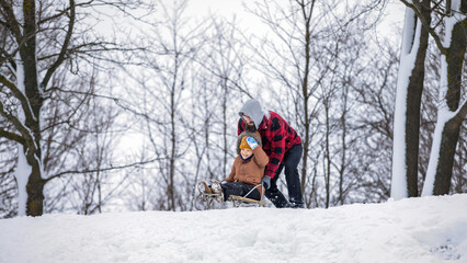 A little boy on a sled outdoors with his father, they are preparing to start from a snow mountain